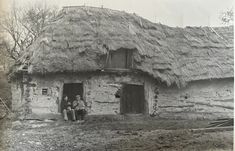 an old black and white photo of two people in front of a thatched house