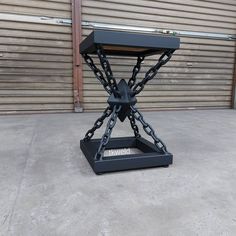 a black metal table with chains on the top and bottom, sitting in front of a garage door