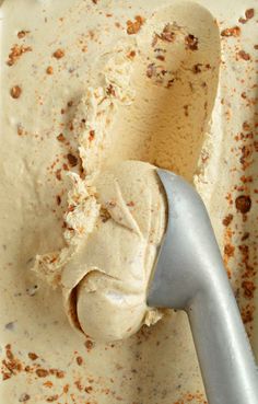 a scoop of ice cream in a bowl with a metal spoon next to it and brown flecks on the surface