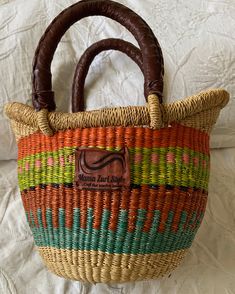 a woven basket with wooden handles on a bed