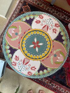 a decorative plate on the floor next to a rug and flowers in vases with one person's feet resting on it