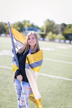 a young woman holding a flag on top of a football field with grass and trees in the background