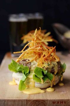 a hamburger with cheese and lettuce on it sitting on a cutting board next to a glass of beer