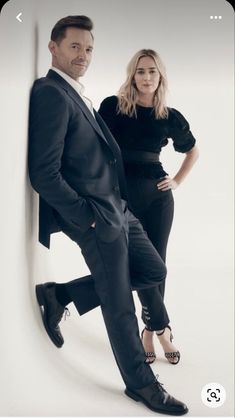 a man and woman posing for a photo in front of a white wall with their hands on the hips