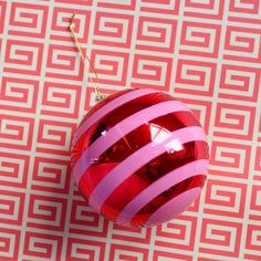 a red and pink ornament hanging from a gold chain on a patterned background