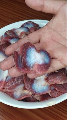 a person holding their hand over some meat in a white bowl on a wooden table