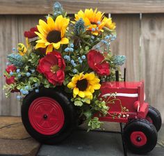 a red wagon with sunflowers and other flowers in it sitting on a table