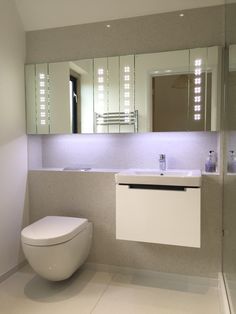 a white toilet sitting next to a bathroom sink under a mirror with lights on it