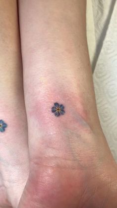 two people with matching tattoos on their legs, both have small blue flowers on them