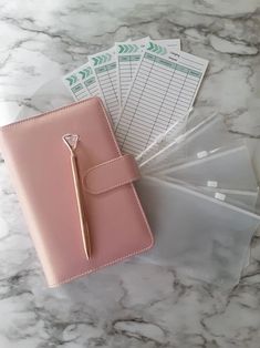 a pink planner and pen sitting on top of a marble table next to some clear bags