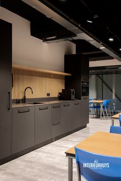 an empty kitchen and dining area with blue chairs in the foreground, along with black walls