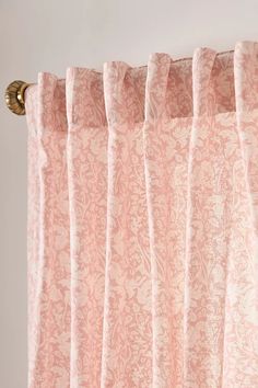 a pink curtain hanging on the side of a window with an ornate pattern and gold hardware