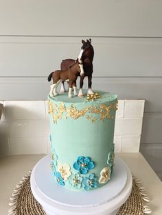 two horses on top of a blue and gold cake with white flowers in the middle