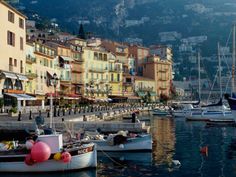 several boats are docked in the water near some buildings and mountains on either side of the bay