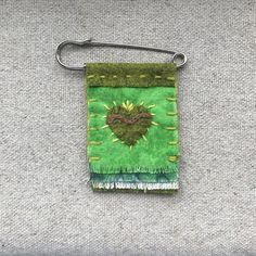 a piece of cloth hanging from a metal hook on a gray surface with green and yellow fringes