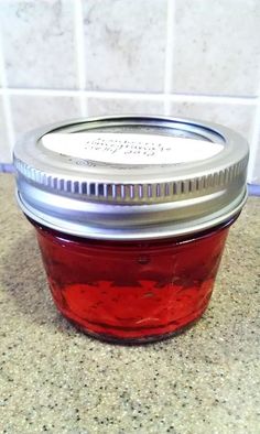 a glass jar filled with red liquid sitting on top of a counter next to a tile wall