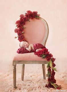 a baby sleeping on top of a pink chair surrounded by red roses and greenery