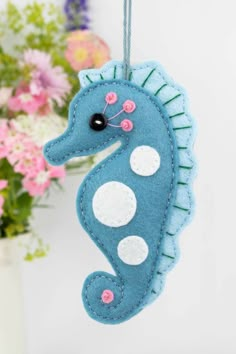 a blue sea horse ornament hanging from a string with flowers in the background