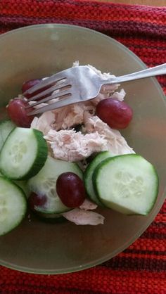 a plate with cucumbers, grapes and chicken on it next to a fork