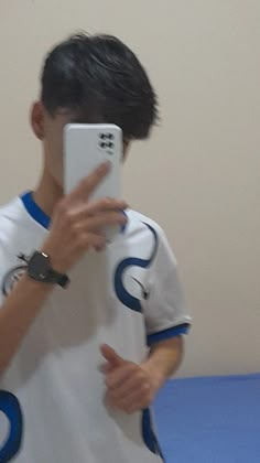 a young man taking a selfie in front of his cell phone wearing a white and blue shirt