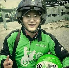 a young man wearing a helmet and holding a green motorcycle helmet with the words go jek on it