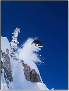 a man flying through the air while riding a snowboard down a snow covered slope