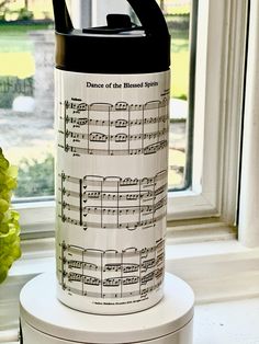 a canister with musical notes on it sitting next to a flower pot and window