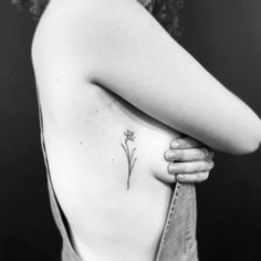 a woman's back with a small flower tattoo on her left side ribcage