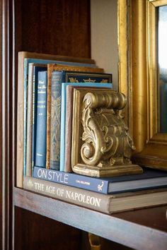 books are stacked on top of each other in front of a gold framed mirror and ornate bookend