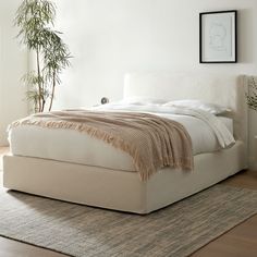 a white bed sitting on top of a wooden floor next to a potted plant