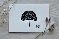 a card with a black leaf on it next to some purple flowers and white paper