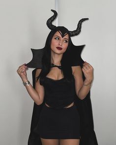 a woman in a black dress with horns on her head is posing for the camera