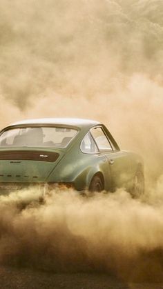 a green car driving through some dust on the road with it's hood up