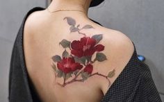 a woman's back tattoo with red flowers and leaves on her left shoulder,