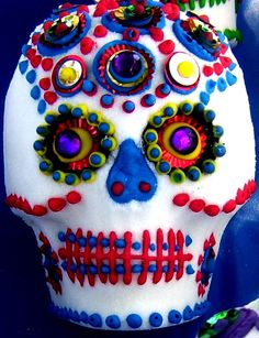 a white skull with colorful decorations on it's face and eyes, sitting in front of a blue background