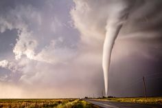 a large tornado is coming out of the sky over an empty road on a cloudy day