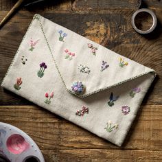 an embroidered clutch bag sitting on top of a wooden table next to scissors and other crafting supplies