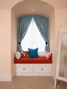 a window seat in the corner of a room with blue drapes and pillows on it