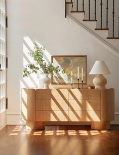 a wooden dresser sitting under a stair case next to a lamp and painting on the wall