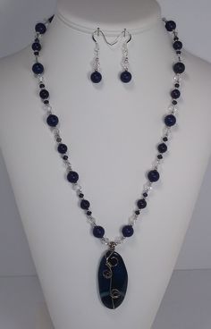 This is a Beautifully Elegant,  23 inch Necklace made with a 2 1/4 inch long x 1 inch wide, wire wrapped Blue striated stone pendant. The Necklace features deep blue, round, Lapis Lazuli beads which alternate between 8mm and 10mm. The smaller round blue beads are 4mm Imperial Jasper beads with 2mm Sterling Silver rounds  between the 6mm crystal clear, sparkling AB (aurora borealis) bicones which add a brilliant shine to the necklace. It is finished off with 4mm Imperial Jasper round beads for comfort around the neck and a Sterling Silver plated Hook and eye clasp for easy connecting. Wire Wrapped Lapis Lazuli Pendant Jewelry, Blue Sodalite Jewelry With Natural Stones, Blue Sodalite Jewelry, Sapphire Gemstone Beads Sodalite Jewelry, Sapphire Gemstone Beads Jewelry In Sodalite, Blue Agate Dangle Jewelry, Lapis Lazuli Wire Wrapped Healing Jewelry, Elegant Round Sodalite Jewelry, Blue Wire Wrapped Round Bead Jewelry