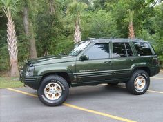 a green suv parked in a parking lot next to trees and palm tree's