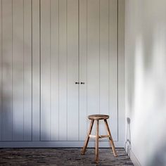 a wooden stool sitting in front of a white wall with wood paneling on it