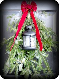 a christmas wreath with a lantern hanging from it's side and a red bow on top