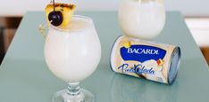 two glasses filled with white liquid and topped with pineapple on the rim, next to a can of bacardi