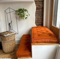 an orange bench sitting in front of a window next to a basket and potted plant