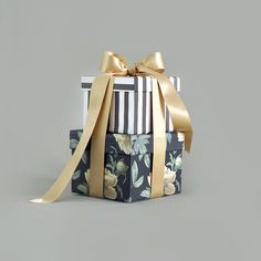 two wrapped gift boxes with gold ribbons and bows on them, both decorated in black and white floral designs