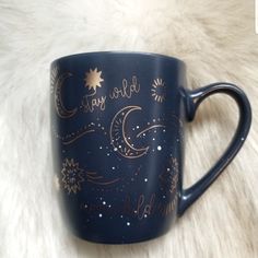 a blue coffee mug with gold stars and moon designs on the side, sitting on a white fur surface