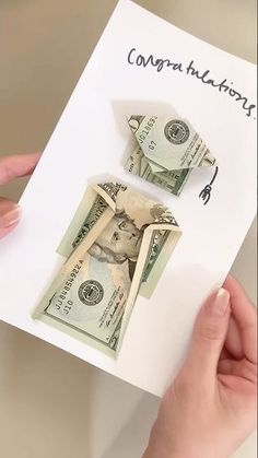 someone is holding up a money origami house on top of a piece of paper