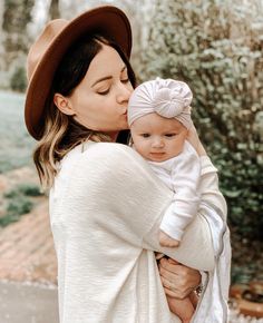 a woman holding a baby in her arms and kissing it's face while wearing a hat