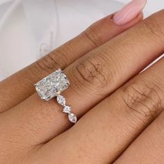 a woman's hand with a diamond ring on top of her finger and the other hand holding an engagement ring